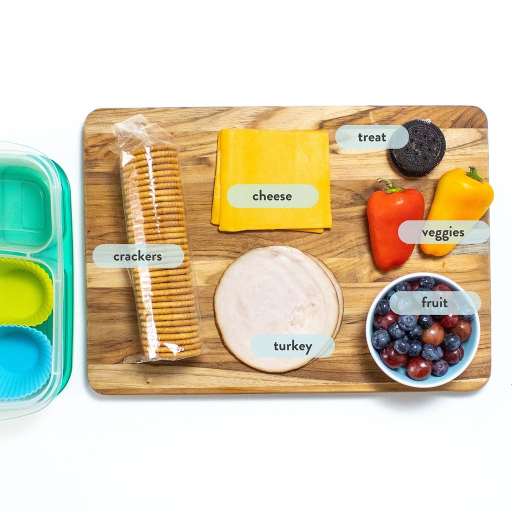 wood cutting board with ingredients spread on top to make turkey lunchables.