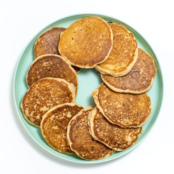 Teal kids plate with a circle of applesauce pancakes on a white background.