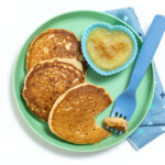 Teal kids plate with 3 applesauce pancakes, a small heart shaped bowl for applesauce, a blue fork and a blue patterned napkin.
