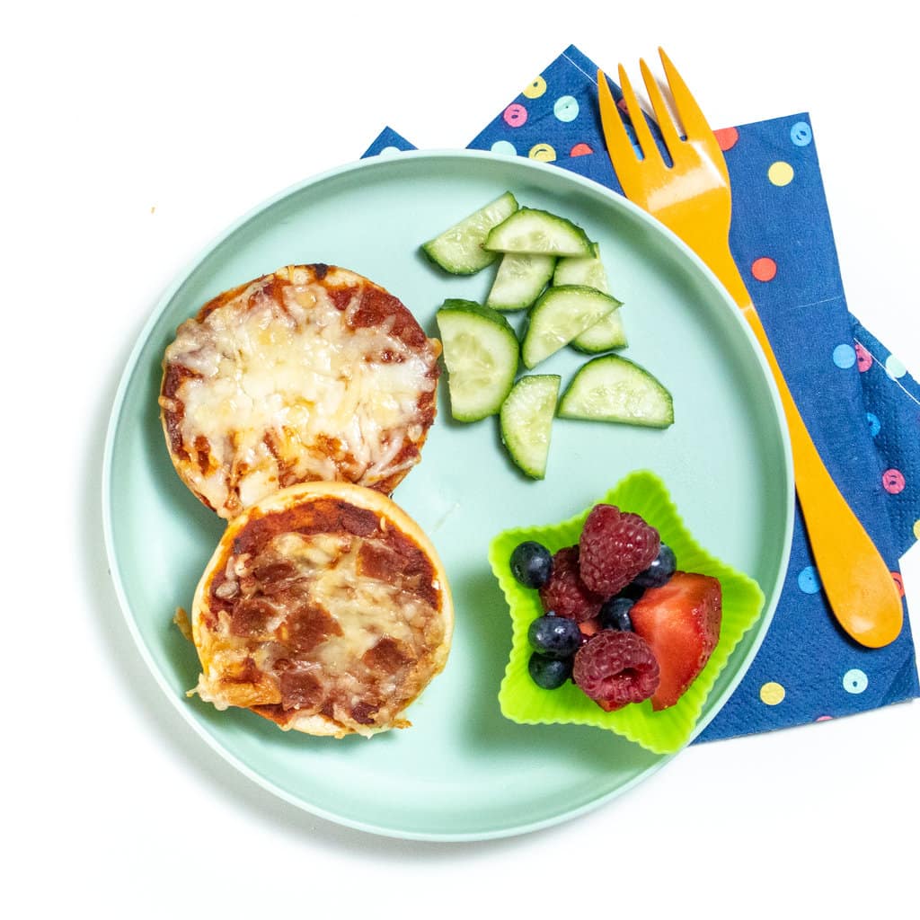 Blue kids plate with bagel bites, cut veggies and fruit and a colorful napkin.