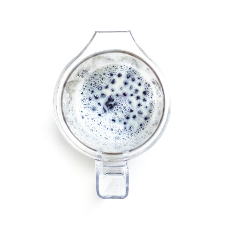 Clear blender on a white counter with blueberries inside.