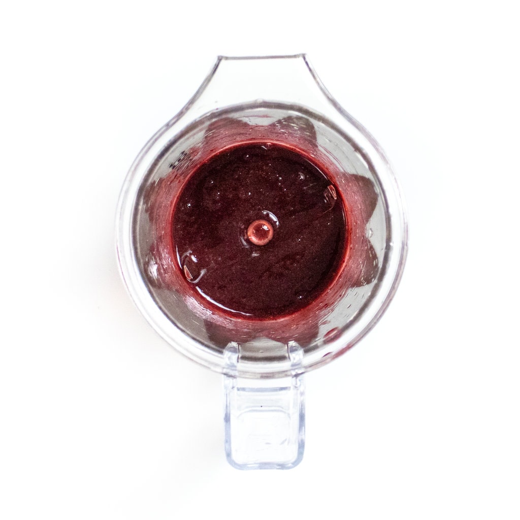 Clear blender with cherry puree on a white counter.