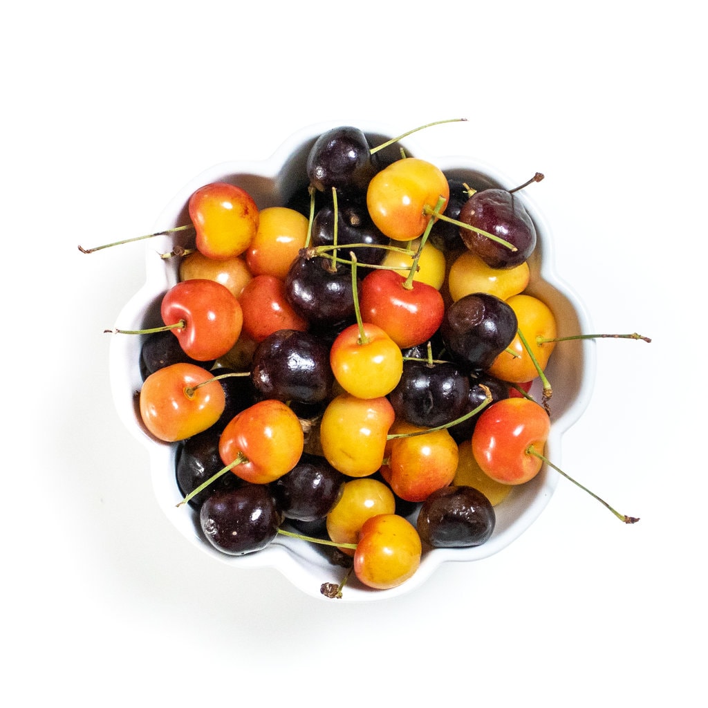White bowl of cherries - both red and white with their stems on a white counter.