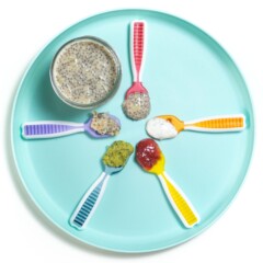 Teal baby plate on a white background with 5 different rainbow colored spoons showing off different ways to serve chia seeds to a baby.