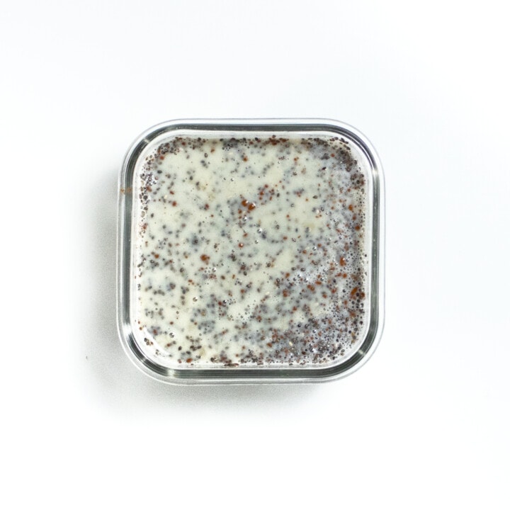 small glass container with the start of chia seed pudding on a white counter.