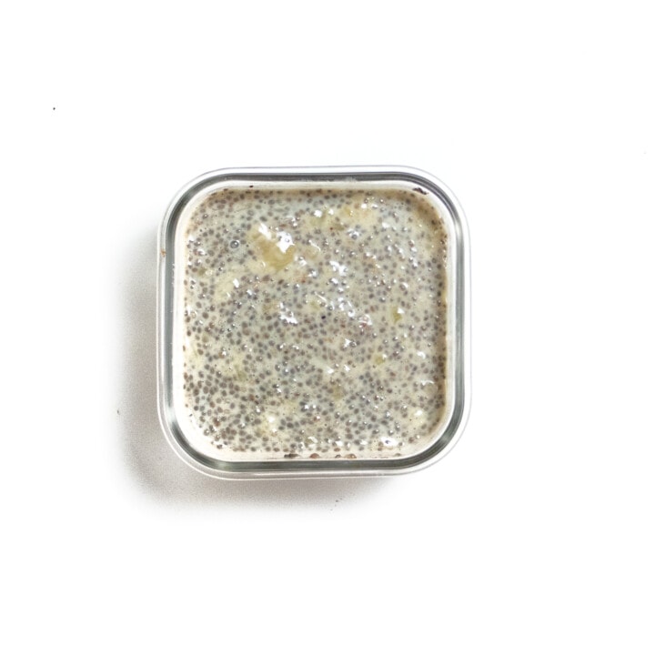 Small glass container with chia seed and banana on white counter.
