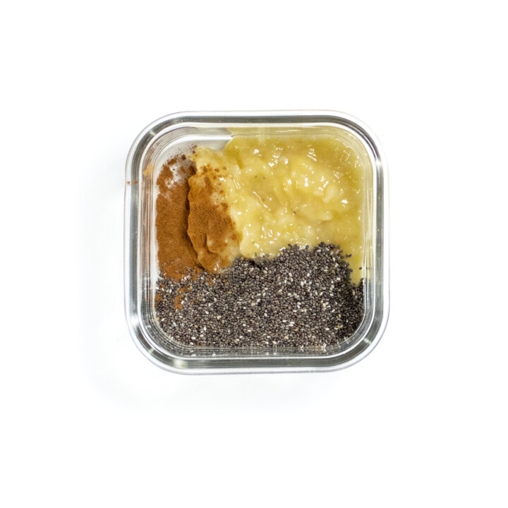 small glass container with chia seeds, mashed banana, cinnamon on a white counter.