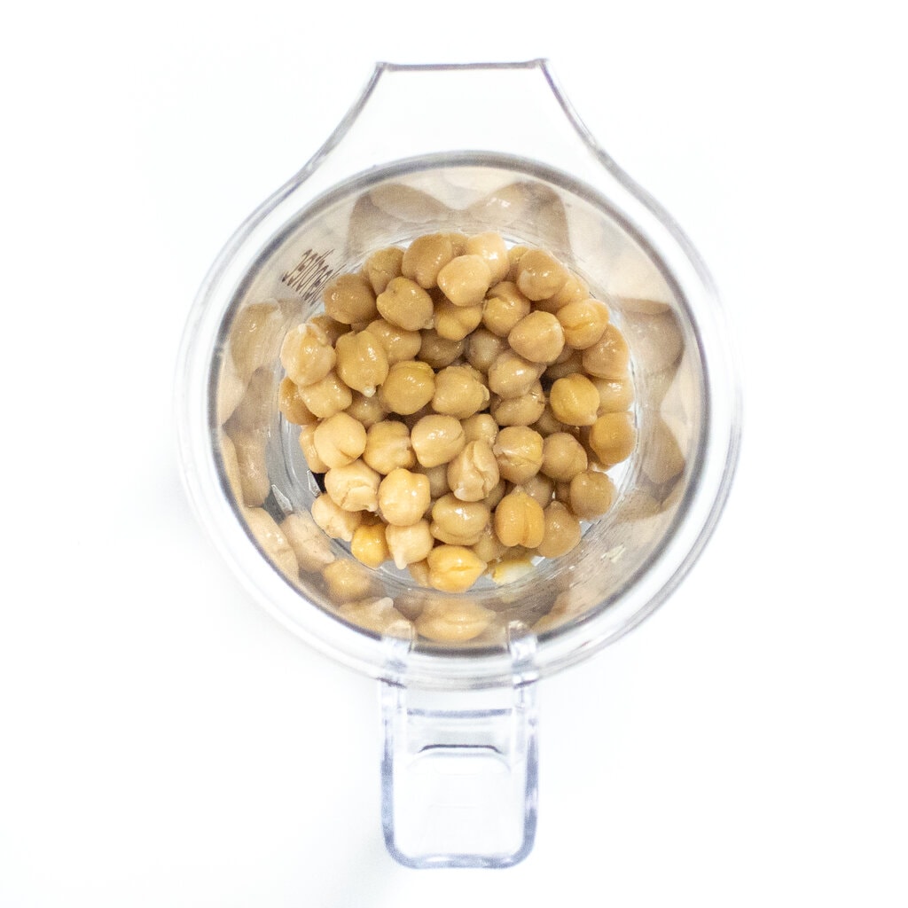 Clear blender with chickpeas on a white countertop.
