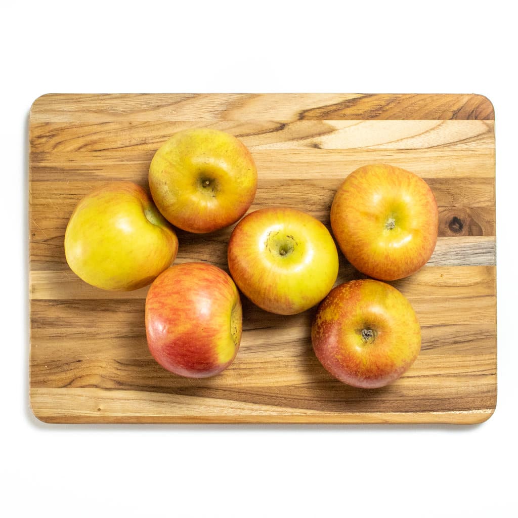 Cutting board with apples on a white counter.