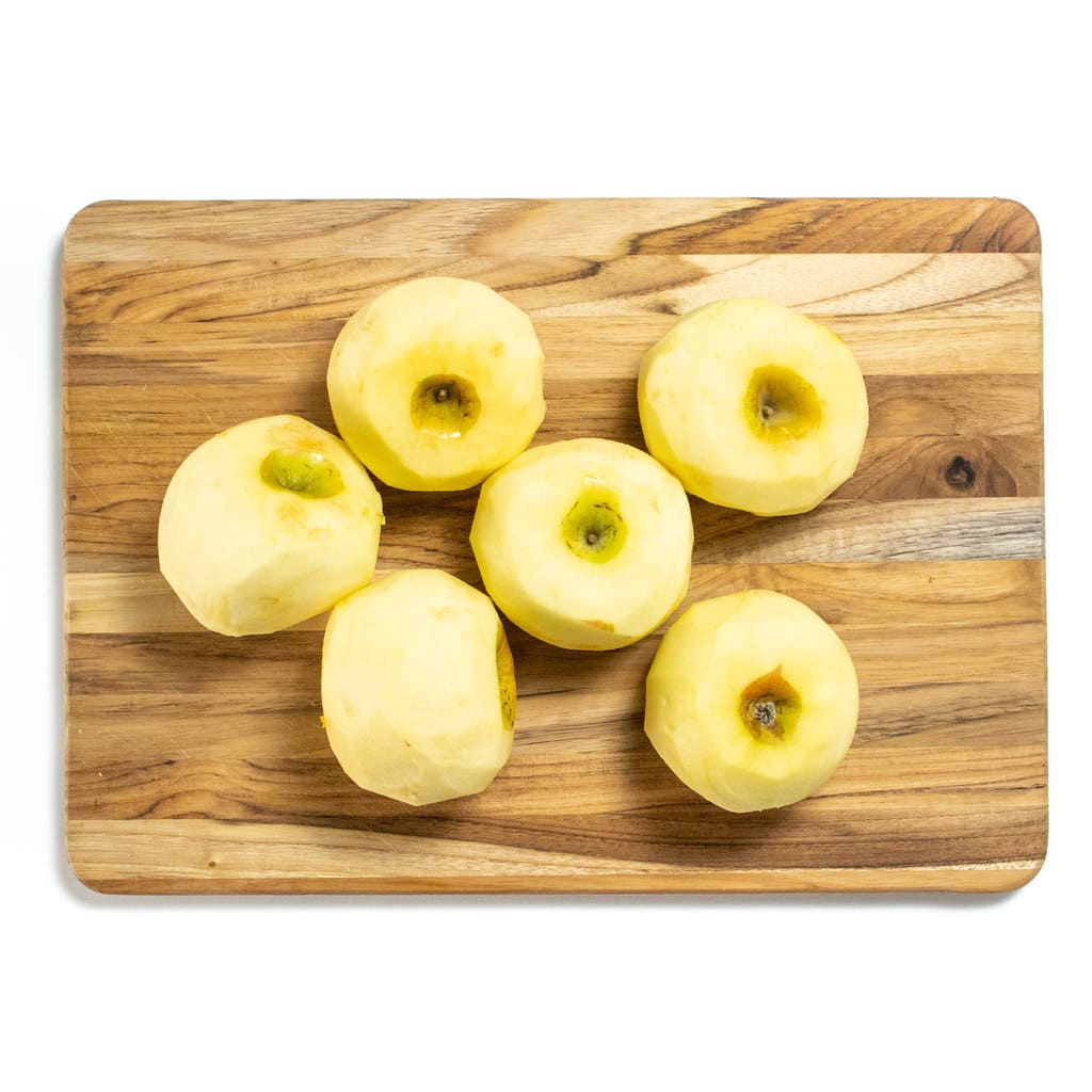 Wooden cutting board on a white counter with peeled apples.