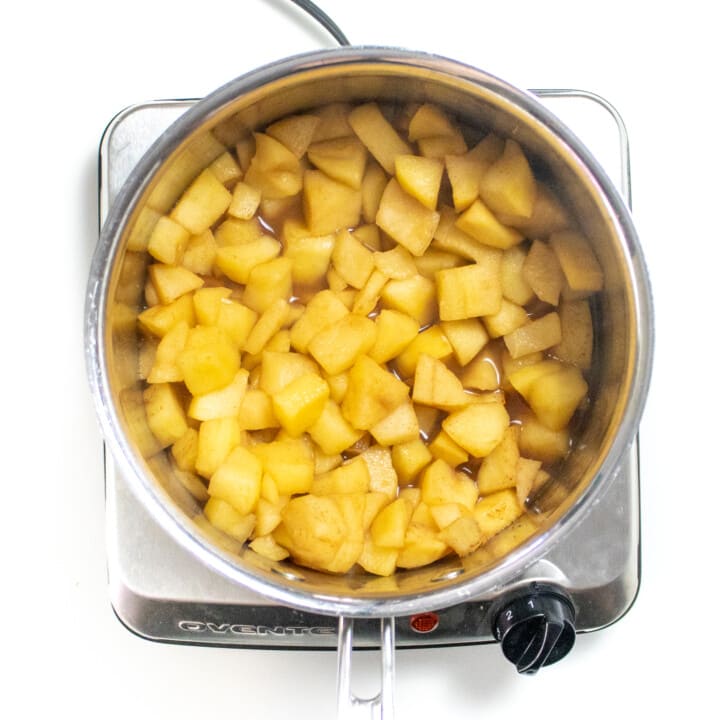 Silver saucepan on a burner with cooked apples and spices.