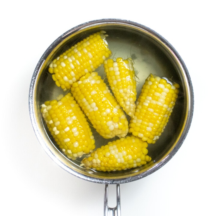A silver saucepan with boiled corn in small pieces.
