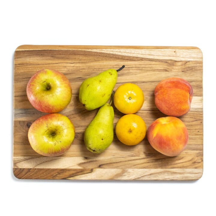 A wooden cutting board with different fruits scattered ontop.