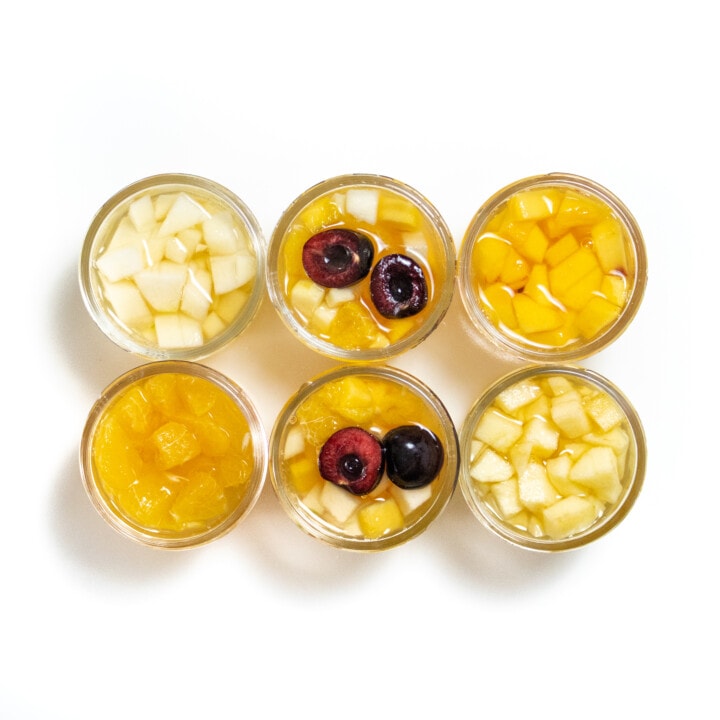 6 small jars filled with different kinds of fruit.