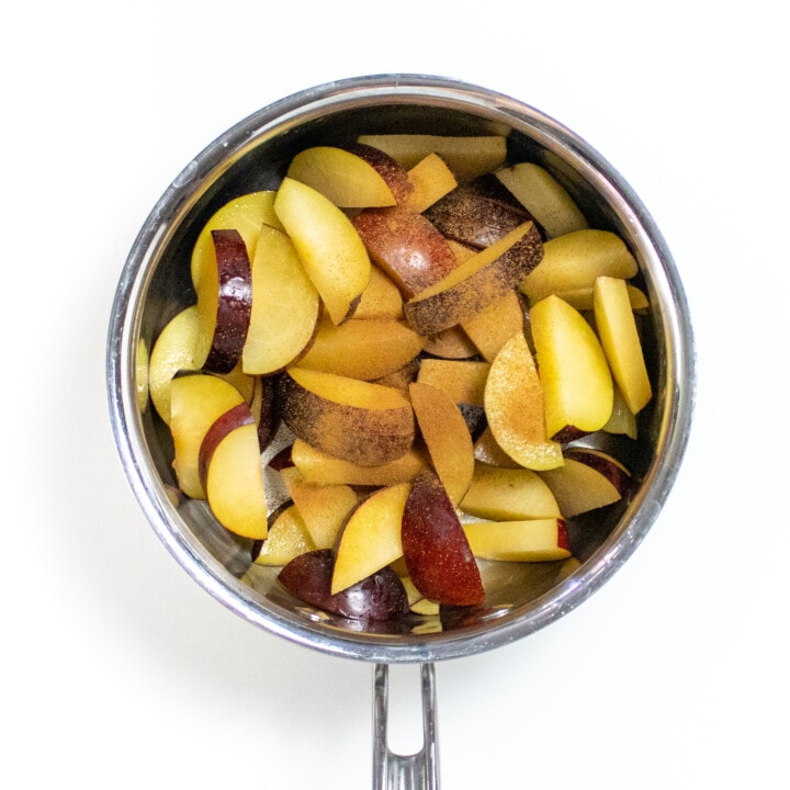 A silver saucepan, with cut plums inside with a pinch of cinnamon.