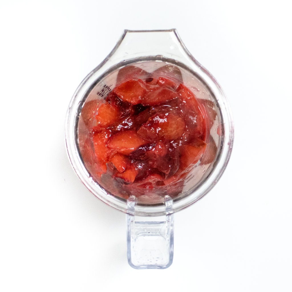 A clear blender on a white counter with cooked plums inside.