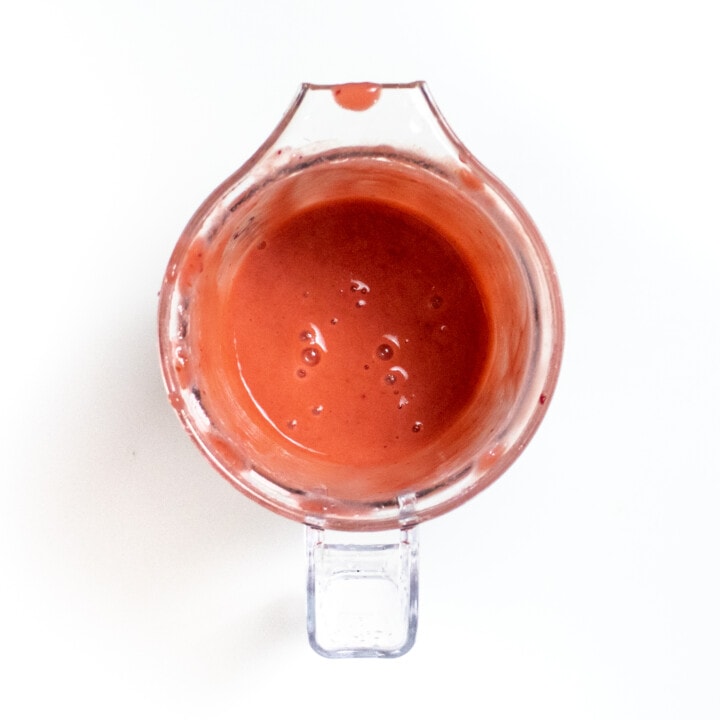 A clear blender with pureed plums inside.