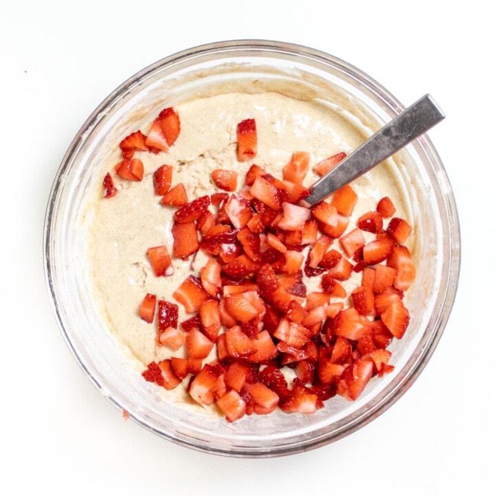 Clear glass bowl with strawberries on top of pancake batter.