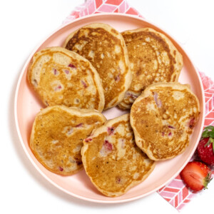 Fanned out strawberry pancakes on a pink kids plate.