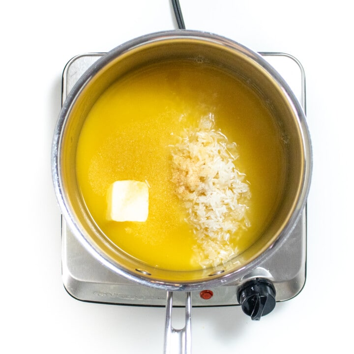 Silver saucepan on a burner with ingredients for cheesy rice.