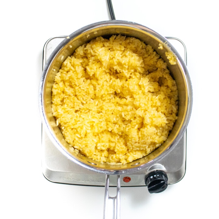 Fluffy cheesy rice in a silver saucepan against a white counter.