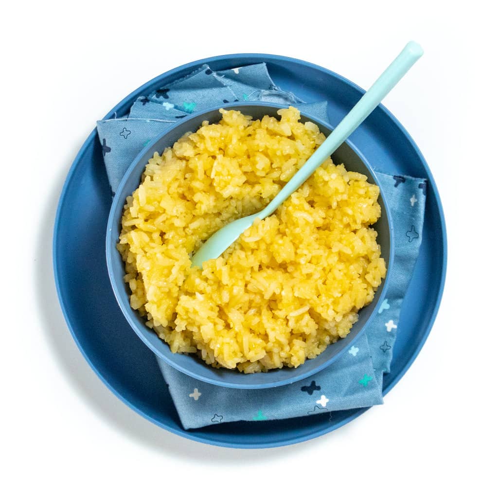 Kids blue bowl and plate with fluffy cheese rice inside with blue spoon resting on top. 