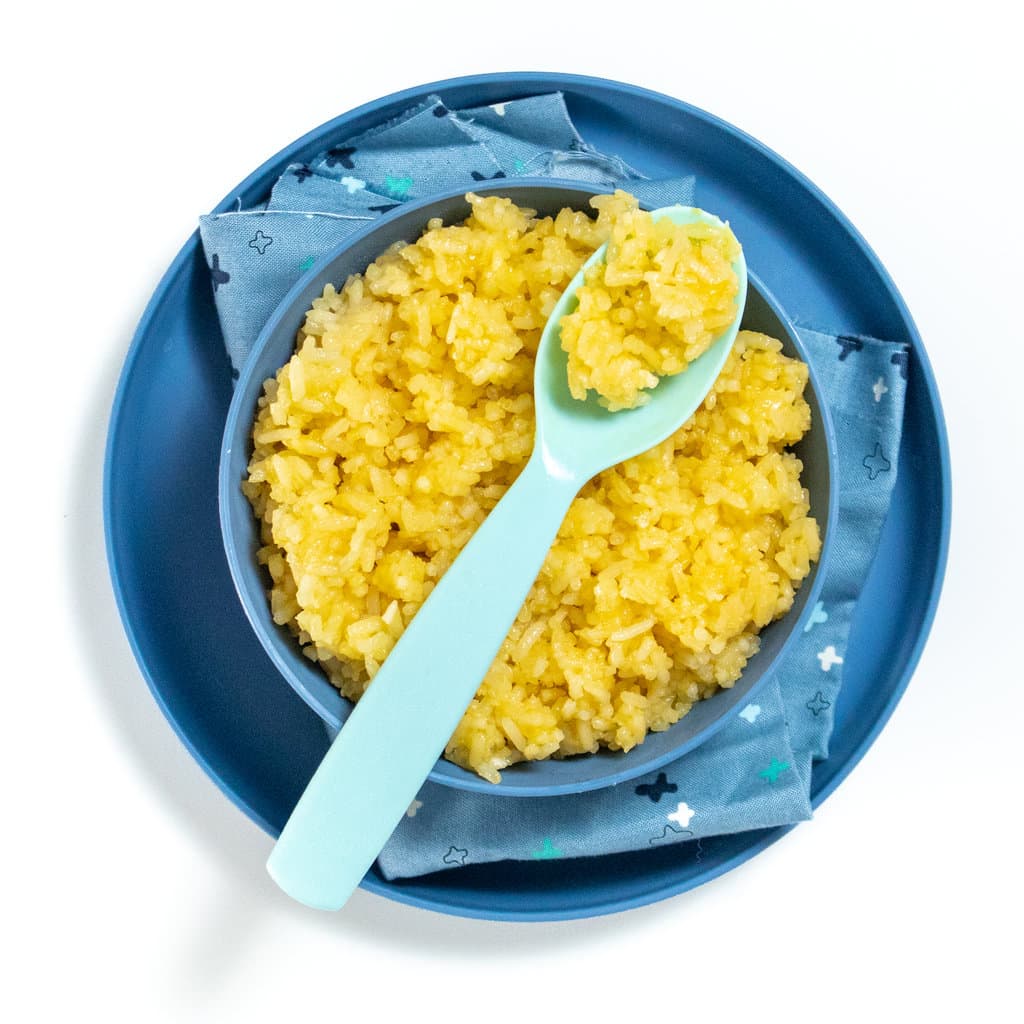 Kids blue bowl and plate with fluffy cheese rice inside with blue spoon resting on top.