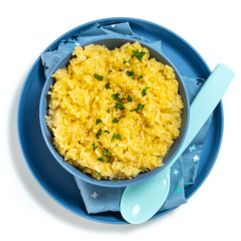 Blue kids bowl and plate with kids cheesy rice inside on a white counter.
