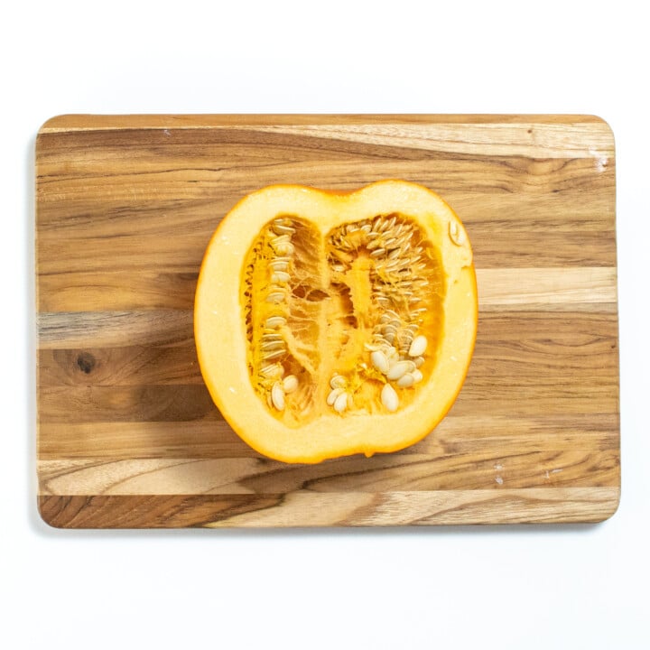 A half of a pumpkin sitting on a wood cutting board on a white counter.