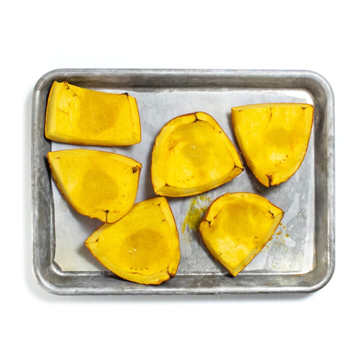 Silver baking sheet with chunks of roasted pumpkin, sitting on a white counter.