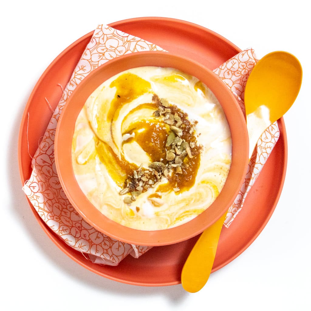 Orange kids plate and bowl with pumpkin yogurt swirled on top sitting on top of a white counter.