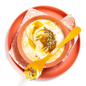 Orange bowl and plate with patterned napkin full of yogurt and pumpkin puree.