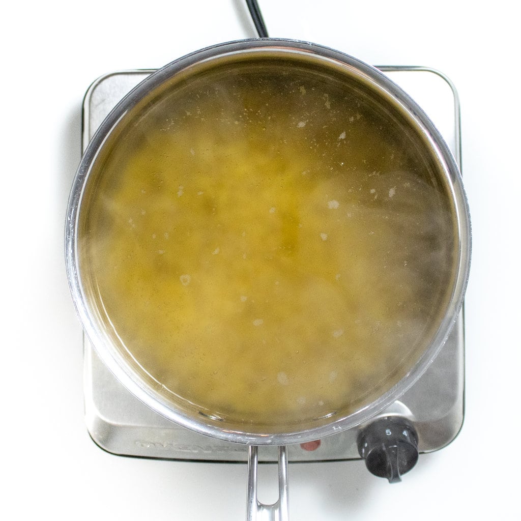 A silver sauce, pan, full of boiling water and pasta against a white background.