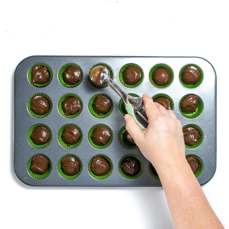 A hand scooping brownie batter into mini muffin tin.