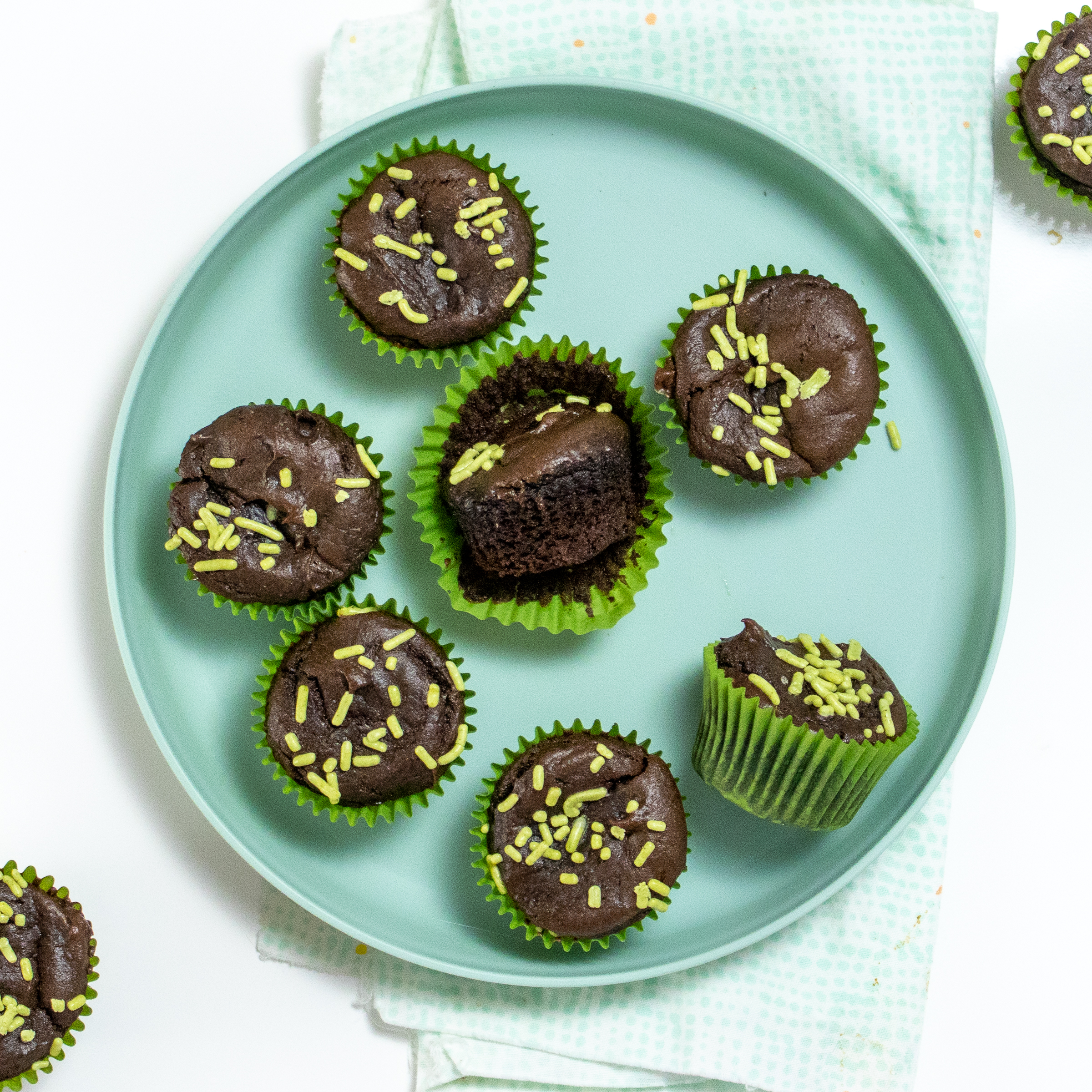 A teal plate with brownie bites with green sprinkles and a blue and green napkin.