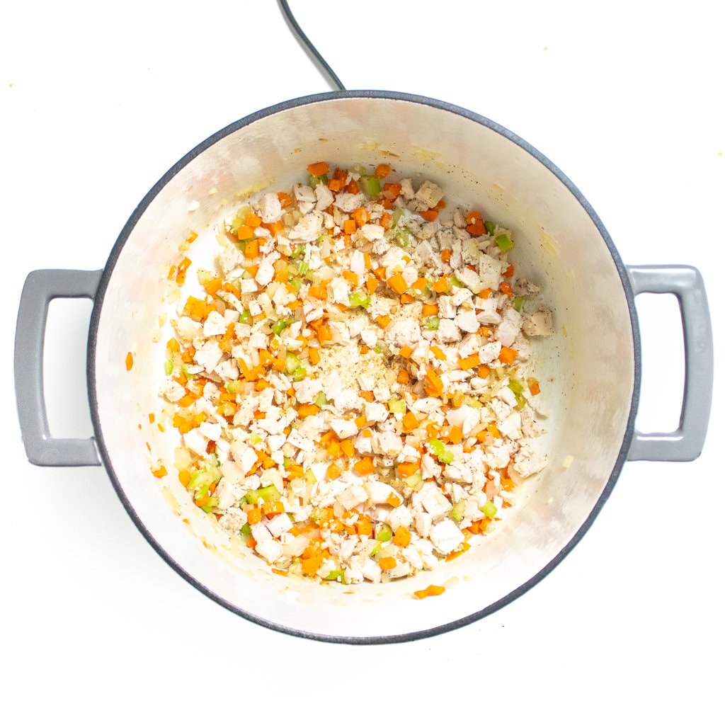 Large gray stockpot on a white countertop with cooked carrots, celery onion, chicken, and spices.