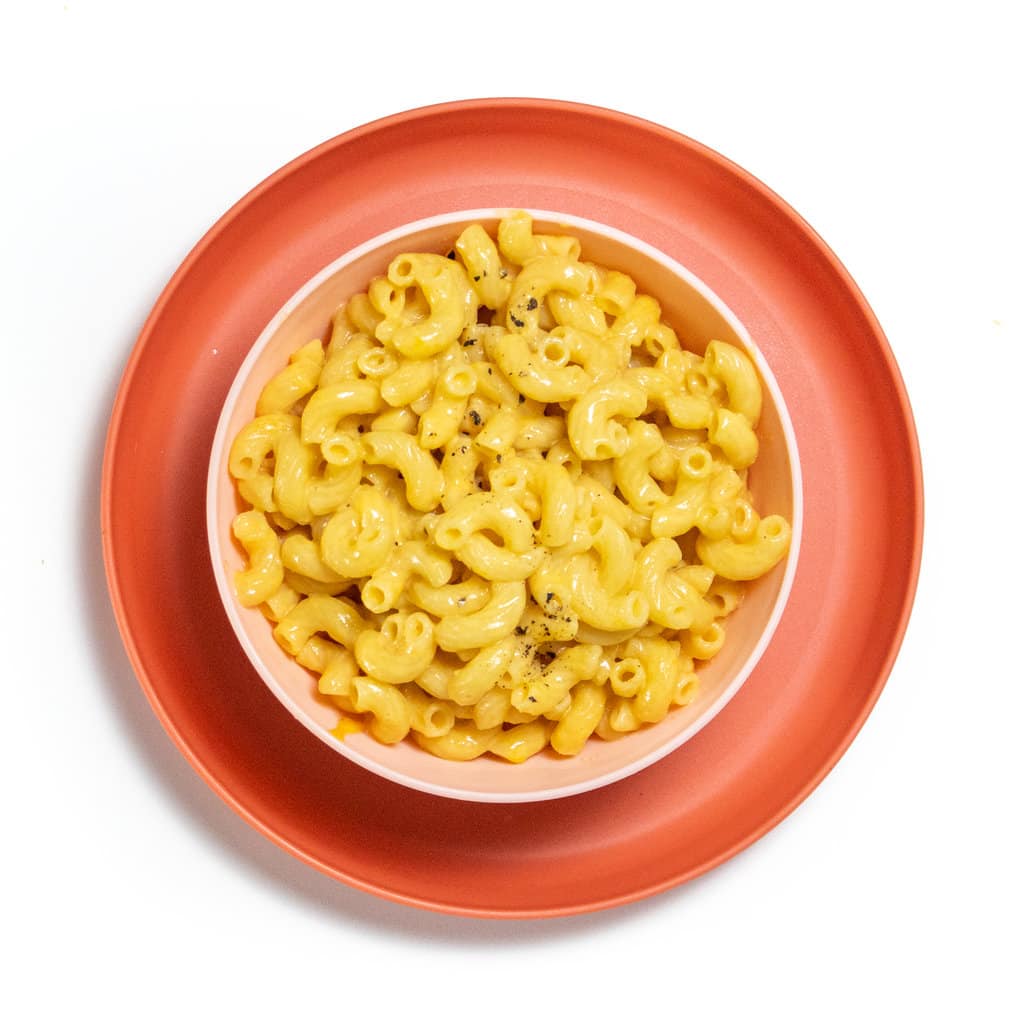 Pink, kids plate, and bowl with veggie mac & cheese with a sprinkle of pepper on top.