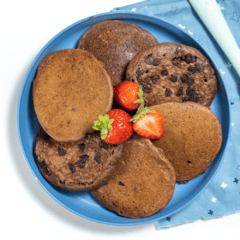 Blue kids plate with a circle of chocolate pancakes with strawberries sitting on a white counter with a blue napkin.