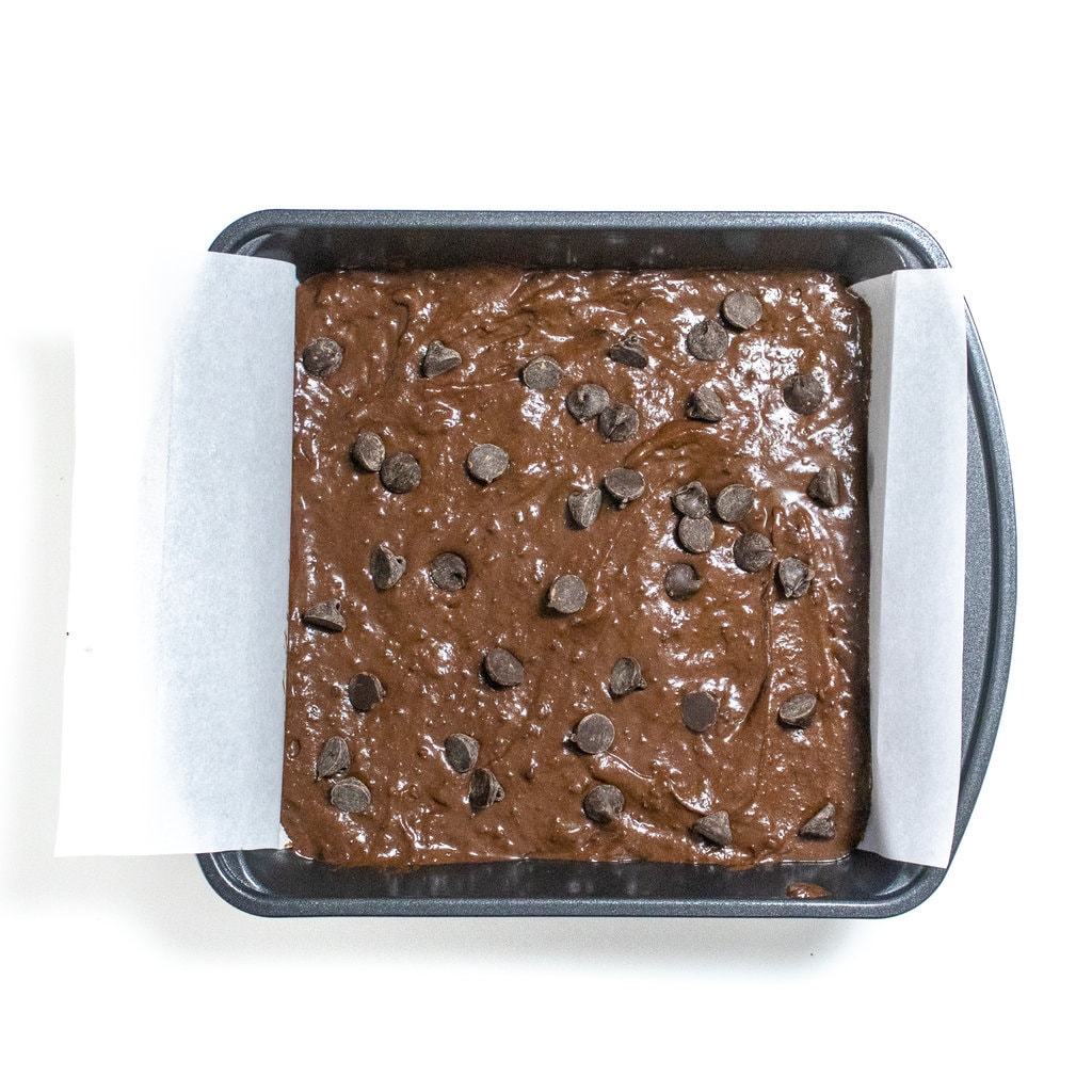 Square baking pan with potato brownie batter with chocolate chip sprinkled on top, ready to be baked.