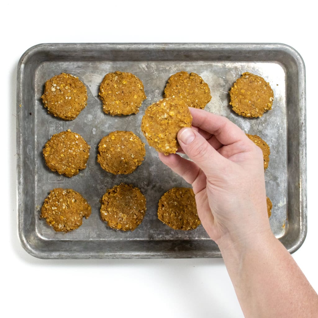 A baking sheet with cooked baby cookies with a hand holding one up.
