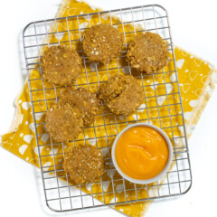 Small cooling rack with cooked sweet potato, baby cookies, and a small bowl of sweet potato purée with a mustard colored napkin on a white countertop.