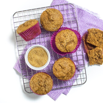 small wire rack with gingerbread muffins in purple wrappers on a purple napkins on a white countertop.