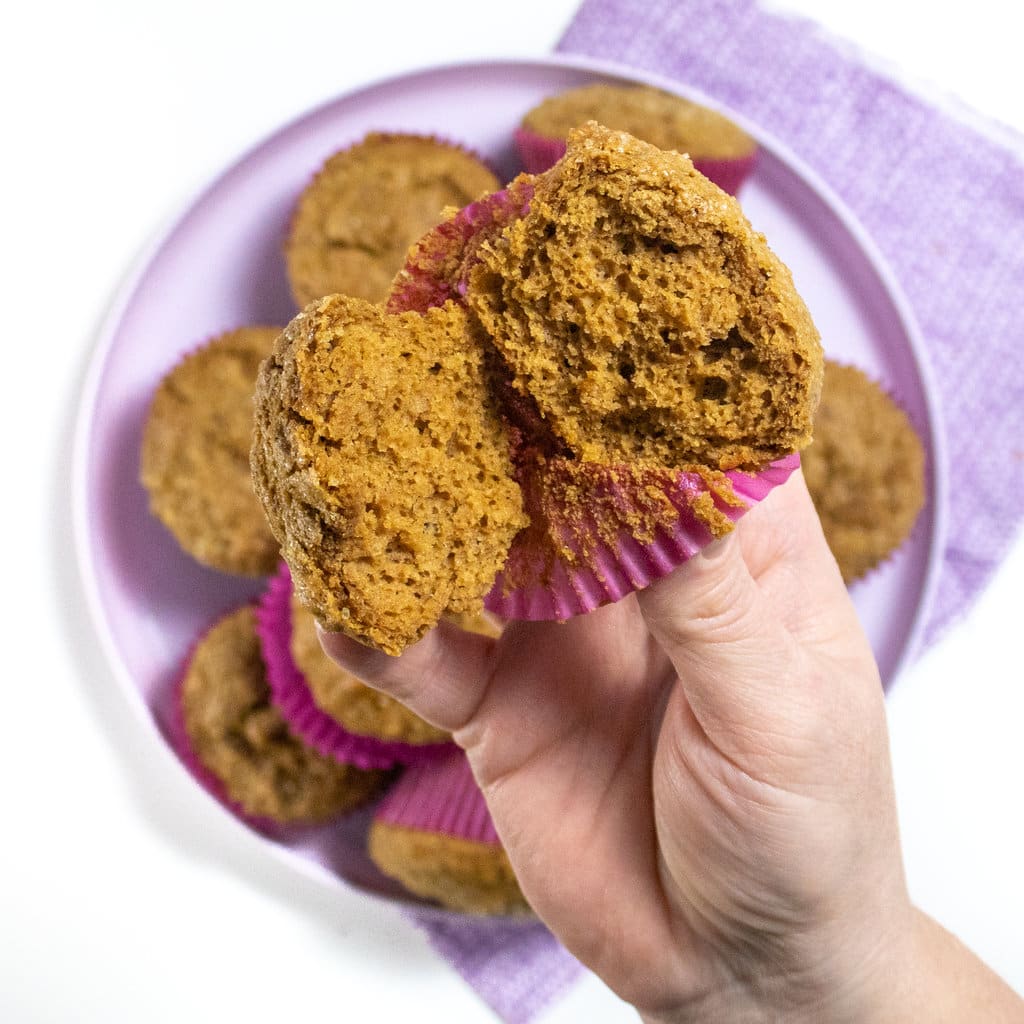 Purple plate with a stack of healthy gingerbread, with a hand holding a cut in half muffin.