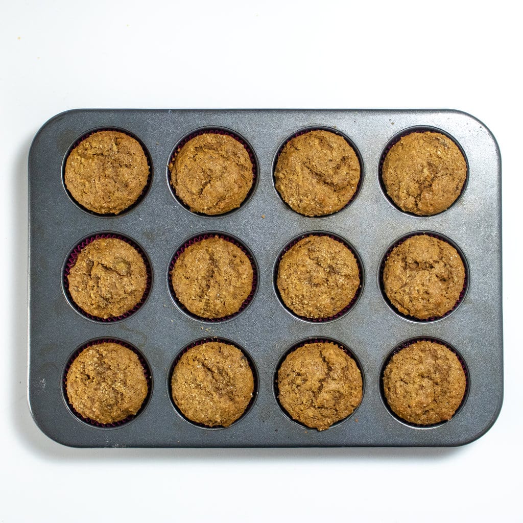 Silver muffin pan with baked gingerbread muffins on a white countertop.