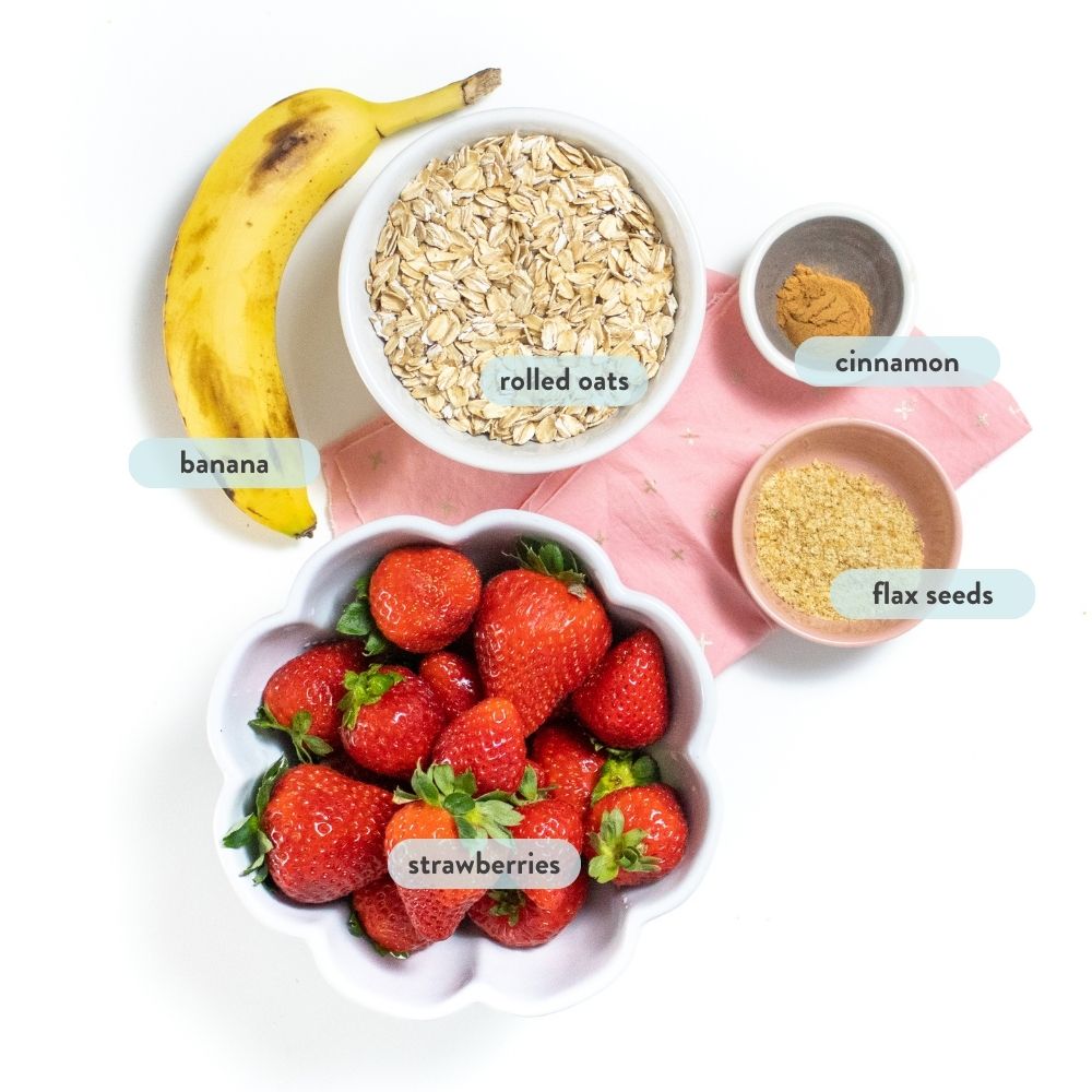 Ingredients for strawberry oatmeal in small bowls on a white countertop with graphics that label the ingredients.