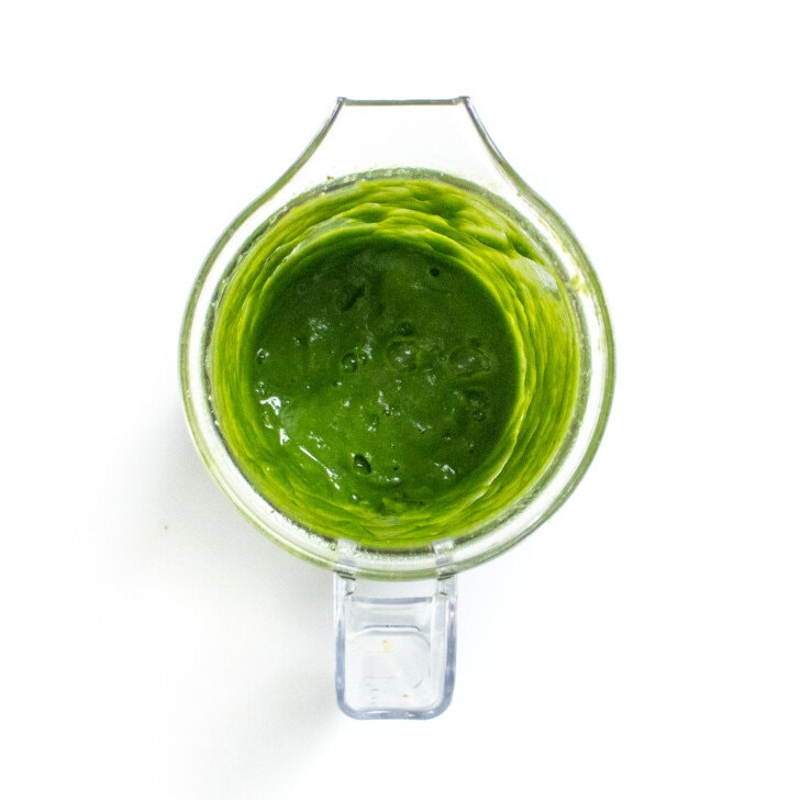A clear blender with puréed kale on away countertop.
