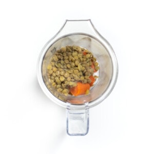 Blender with carrots and lentils on a white counter.