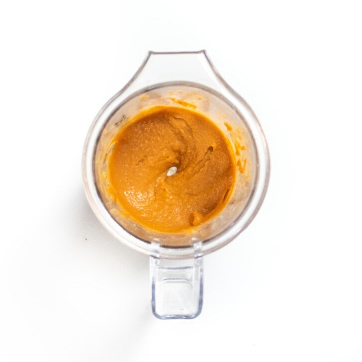Clear blender with pureed carrots and lentils on a white countertop.