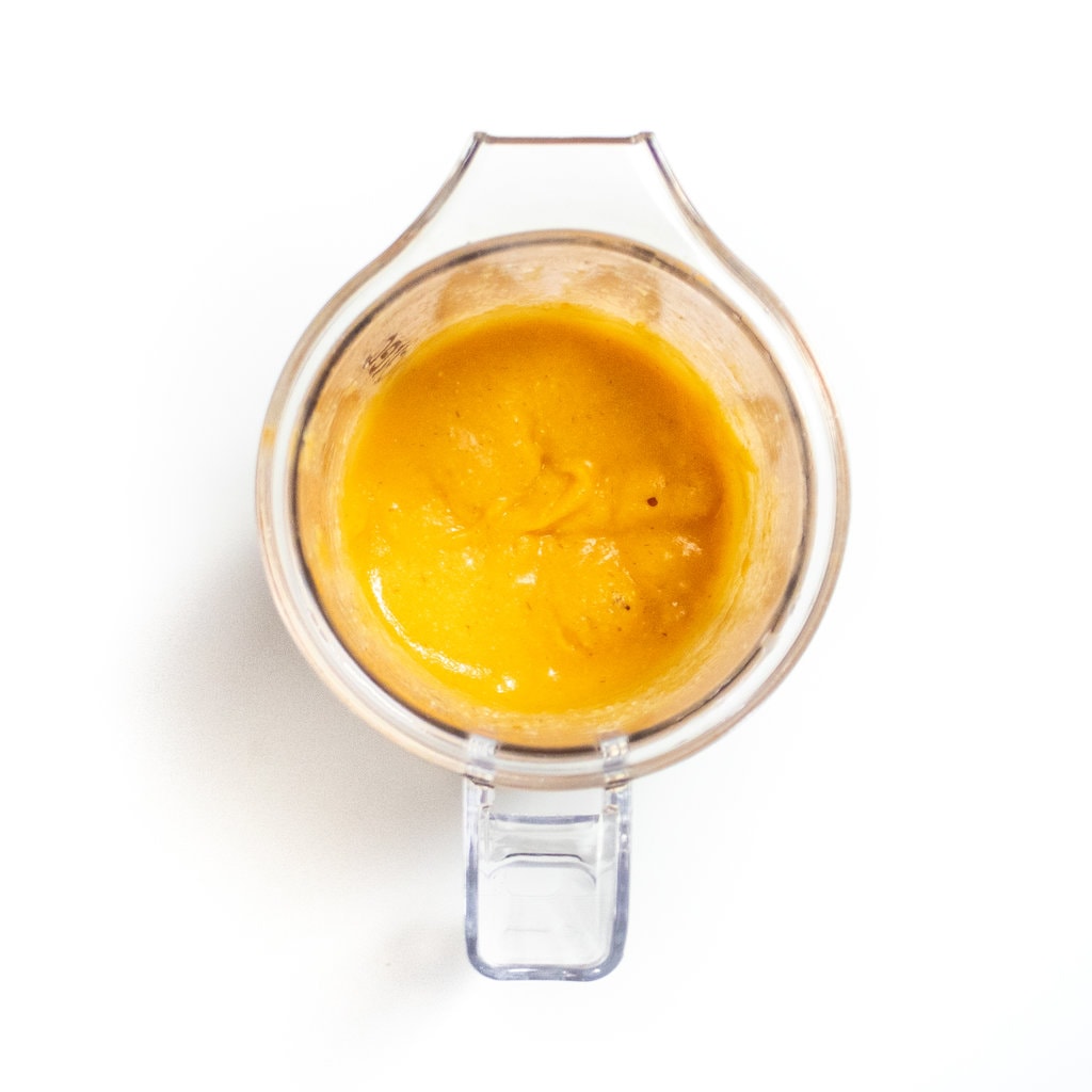 A clear blender, full of puréed carrots, and barley on a white countertop.