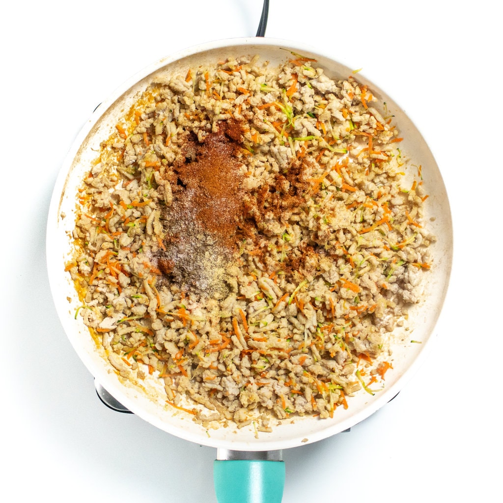 In a medium skillet, there is ground, chicken, grated carrots, grated zucchini, cooking with added, spices – chili powder, paprika, oregano, garlic powder, onion powder, salt, and pepper.